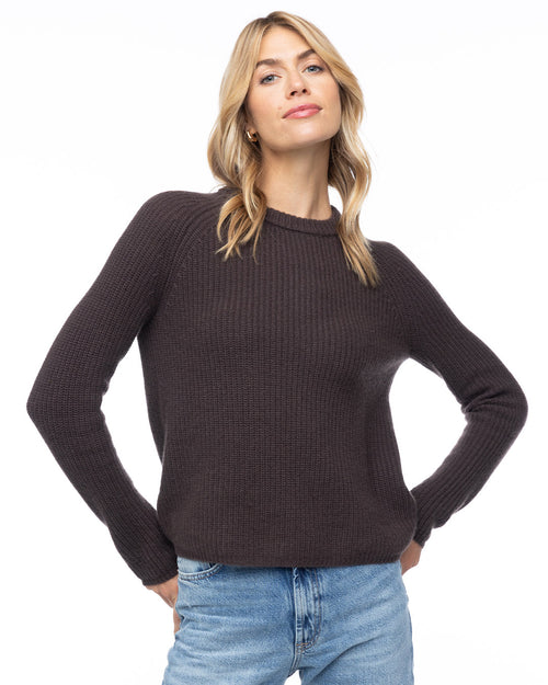 LIFESTYLE / EDITORIAL: Woman wearing dark chocolate ribbed cashmere sweater and blue jeans against white background