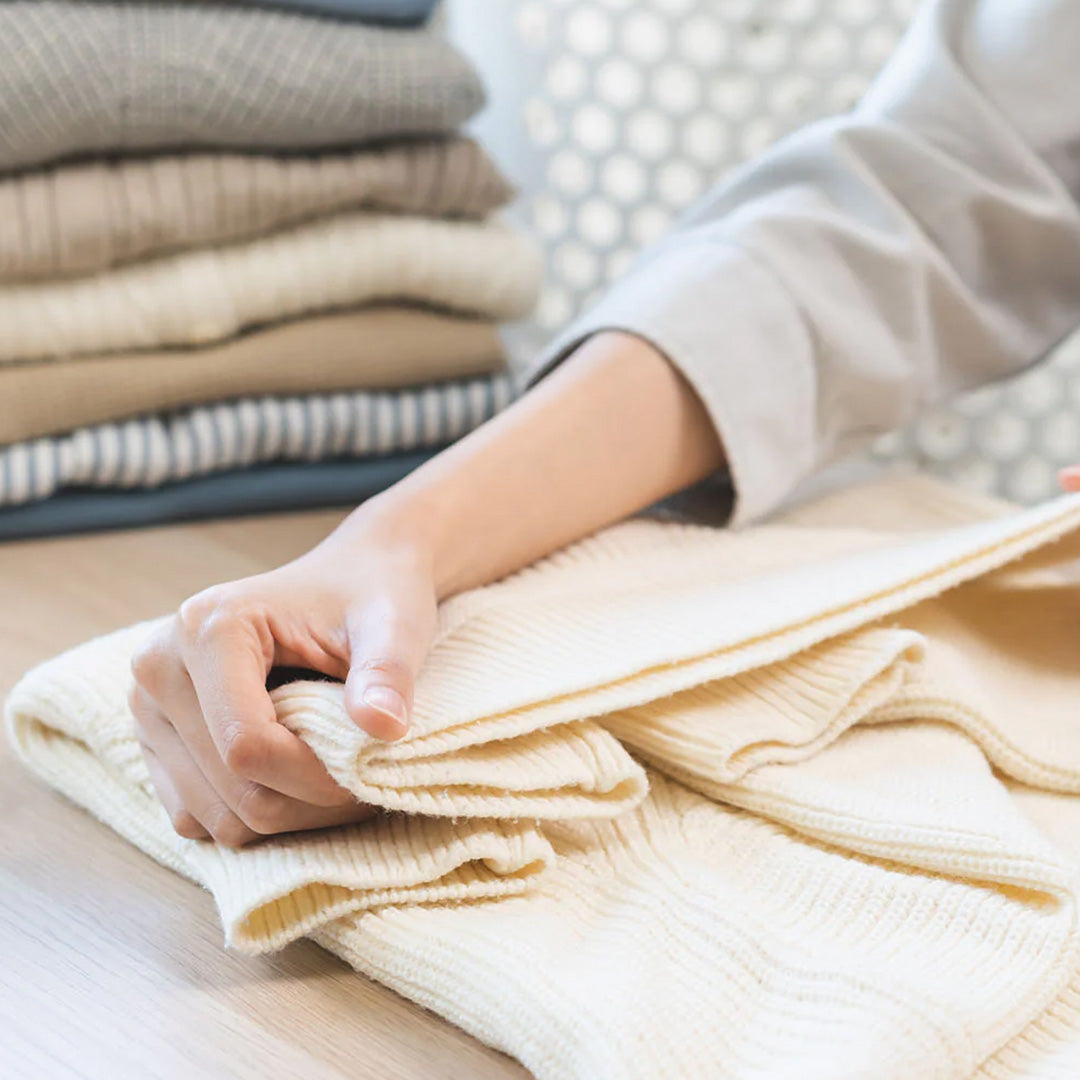 A hand folding a cream ribbed sweater