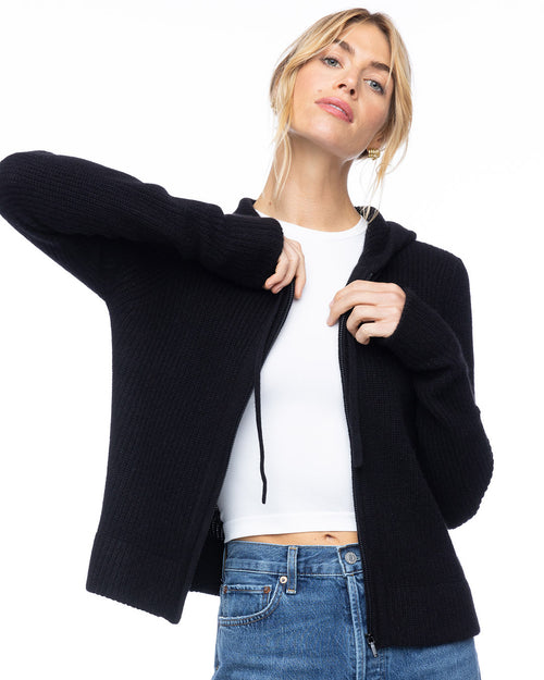 LIFESTYLE / EDITORIAL: Woman wearing black cashmere fisherman hoodie over white top and blue jeans against white background