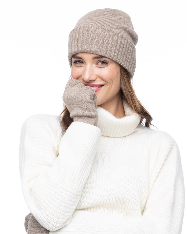 Woman wearing beige cashmere beanie and gloves with white ribbed cashmere turtleneck sweater, smiling, white background