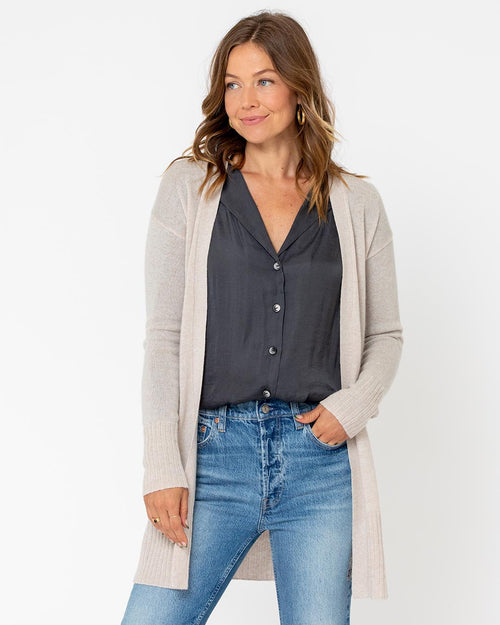 Woman wearing long beige cashmere cardigan over black blouse and blue jeans against white background