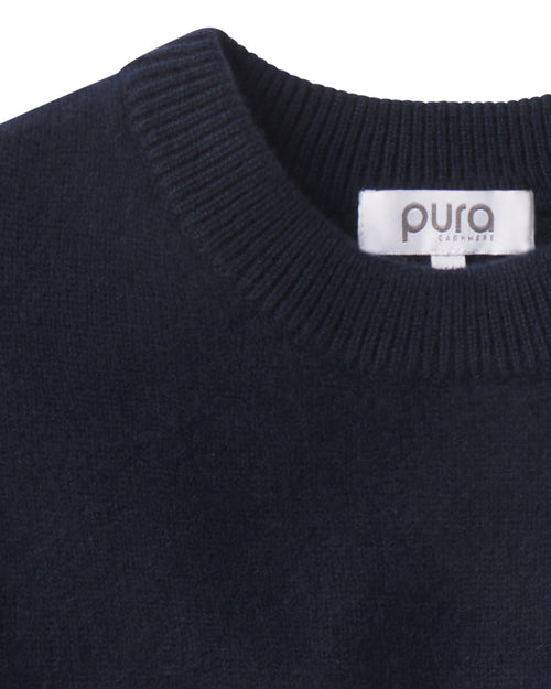Close-up of navy blue cashmere crew neck sweater with visible ribbed collar and brand label "pura cashmere
