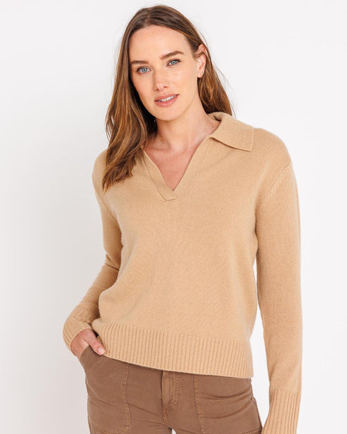 Front-facing image of a woman wearing a camel cashmere polo sweater with collar and brown pants against white background