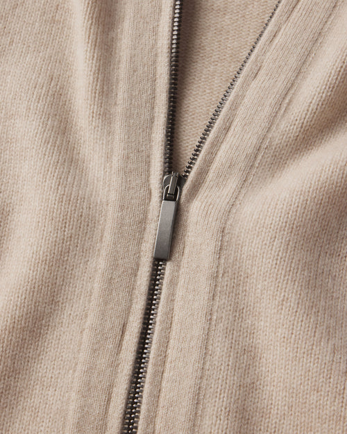Close-up of oatmeal-colored cashmere fabric with a metal zipper partially zipped on a zip-up cardigan