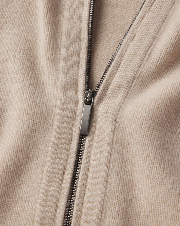 Close-up of oatmeal-colored cashmere fabric with a metal zipper partially zipped on a zip-up cardigan