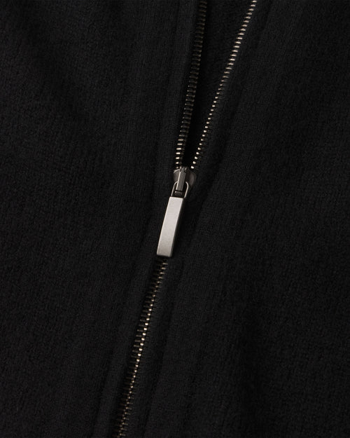 Close-up of black cashmere fabric with partially zipped silver zipper on a zip-up cardigan