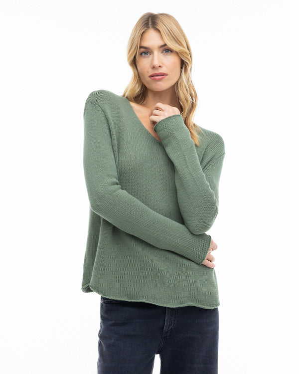 Woman wearing olive green round neck cashmere sweater with long sleeves and dark pants against white background