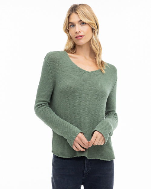 Woman wearing olive green cashmere V-neck sweater with long sleeves and dark pants against white background