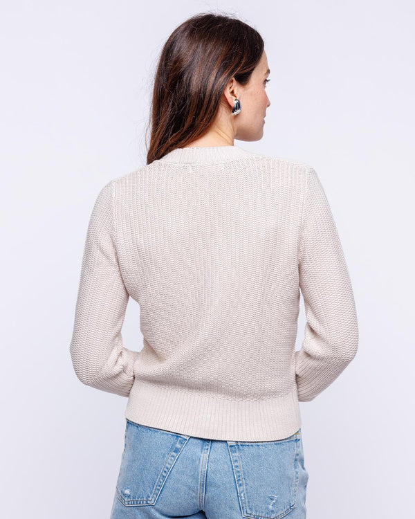 LIFESTYLE / EDITORIAL: Woman wearing oatmeal textured cardigan and light blue jeans, shown from back against white background
