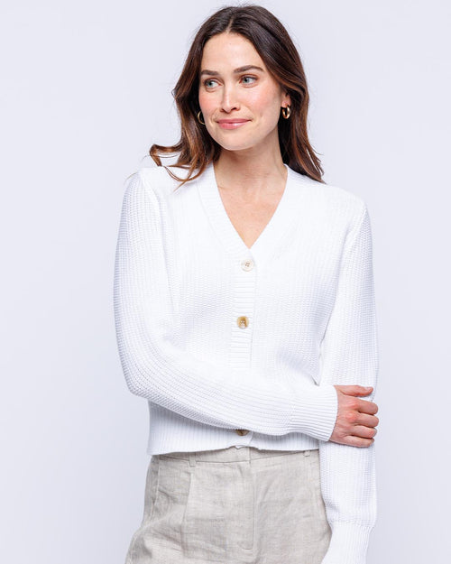 LIFESTYLE / EDITORIAL: Woman wearing white textured cardigan and beige pants against a plain light background