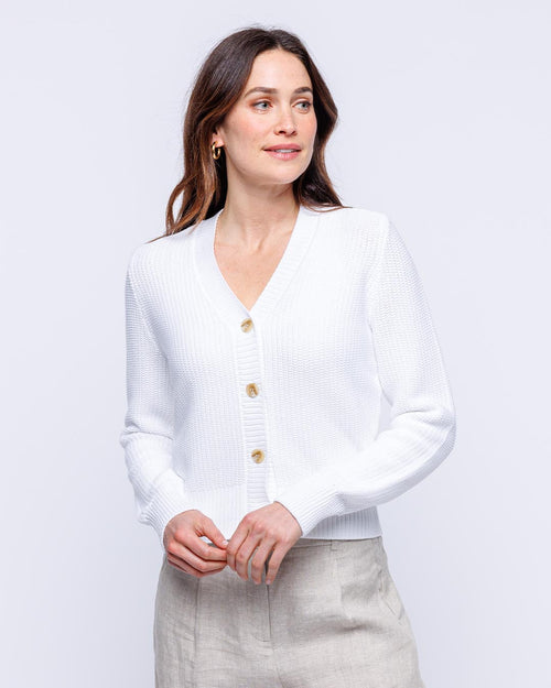 Woman wearing white textured cotton cardigan with buttons, posing against plain light background
