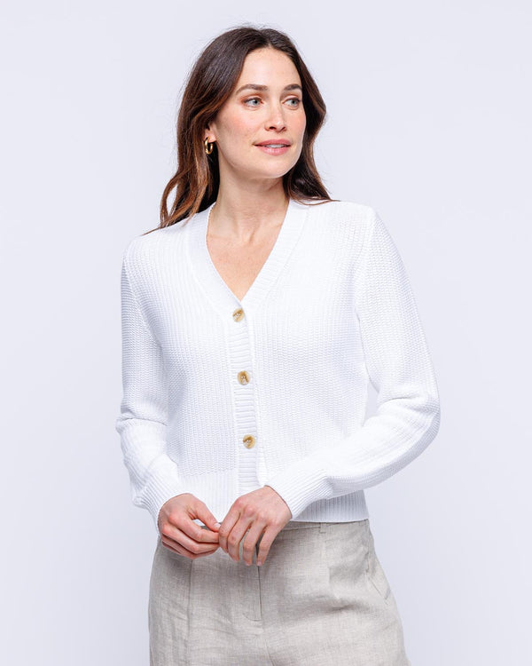 Woman wearing white textured cotton cardigan with buttons, posing against plain light background