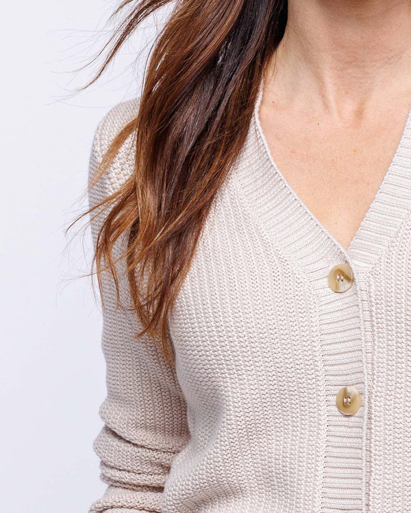 Close-up of oatmeal-colored textured knit cardigan with buttons and long brown hair visible on left side