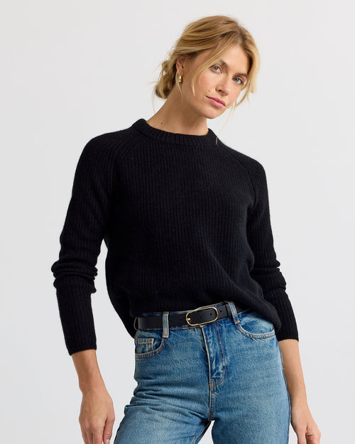 Woman wearing black cashmere sweater and blue jeans against plain background