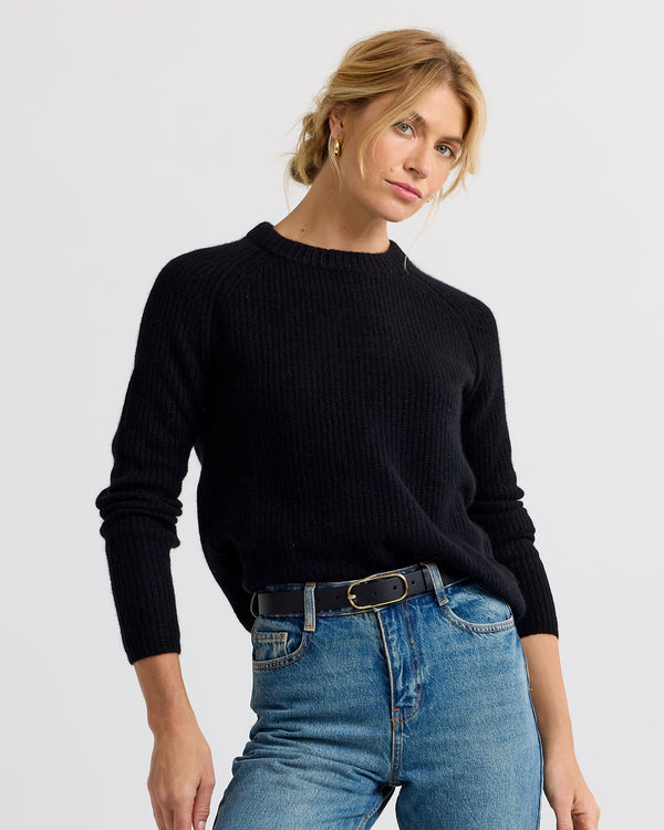 Woman wearing black cashmere sweater and blue jeans against plain background