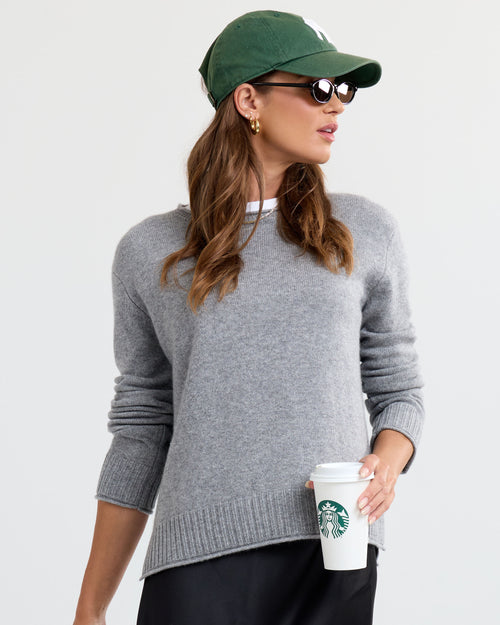 LIFESTYLE / EDITORIAL: Woman wearing gray cashmere sweater, green cap, sunglasses, holding Starbucks cup against white