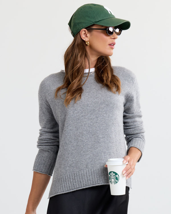 LIFESTYLE / EDITORIAL: Woman wearing gray cashmere sweater, green cap, sunglasses, holding Starbucks cup against white