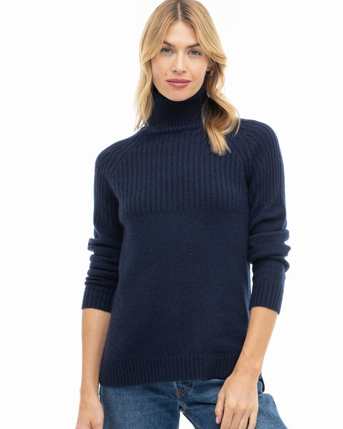 Front view image of a woman wearing a navy blue turtleneck cashmere sweater with jeans against a white backdrop