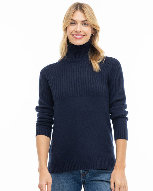 LIFESTYLE / EDITORIAL: Woman wearing navy blue turtleneck cashmere sweater and jeans, smiling against white background
