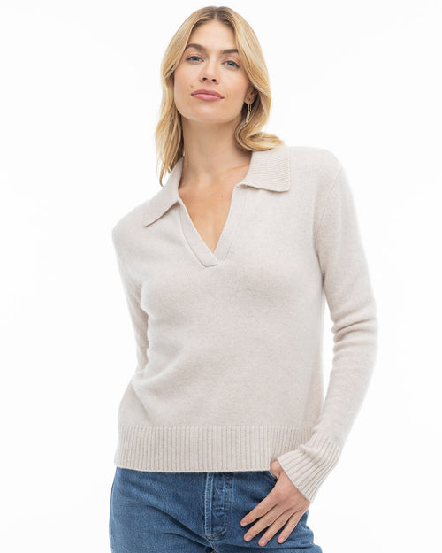 Three-quarter view image of a woman wearing an oatmeal cashmere sweater with collar and V-neck, paired with blue jeans.