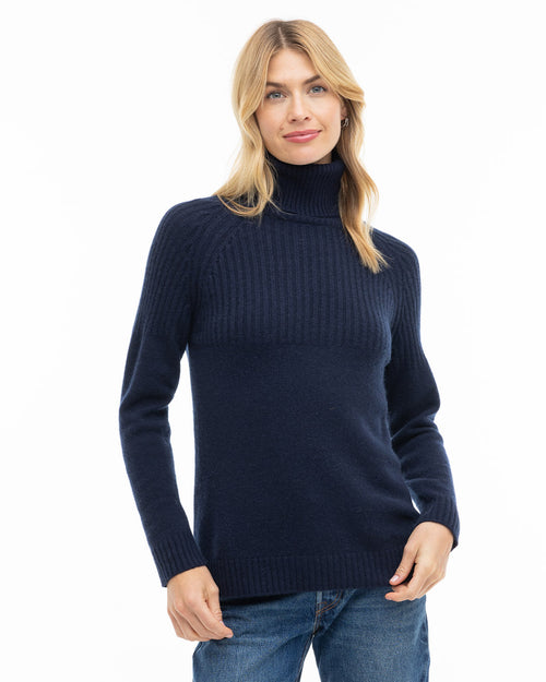 Front view image of a woman wearing a navy blue ribbed turtleneck cashmere sweater and blue jeans