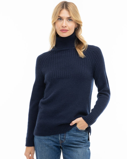 LIFESTYLE / EDITORIAL: Woman wearing navy ribbed turtleneck cashmere sweater and blue jeans, standing with hand in pocket