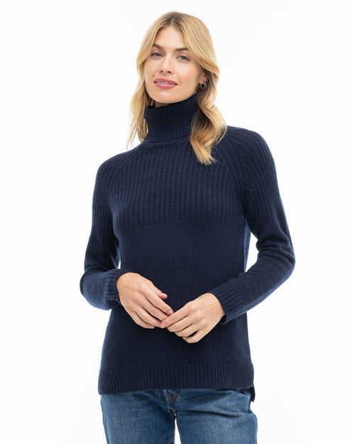 Front view image of a woman wearing a navy blue cashmere turtleneck sweater paired with jeans against white background