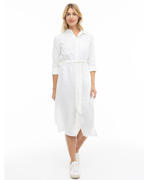 Woman wearing white button-down midi dress with belt and sneakers, standing against white background
