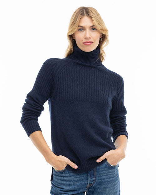 LIFESTYLE / EDITORIAL: Woman wearing navy blue ribbed turtleneck cashmere sweater and jeans, hands in pockets, white