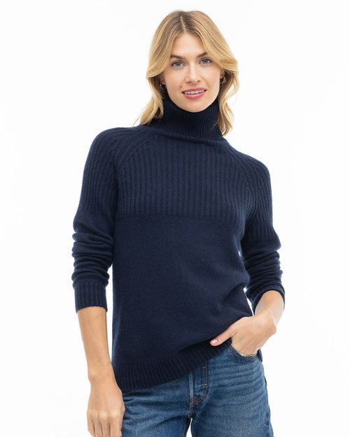 LIFESTYLE / EDITORIAL: Woman wearing navy blue turtleneck cashmere sweater and jeans, standing with hand in pocket