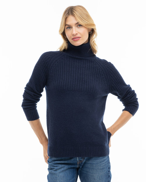 LIFESTYLE / EDITORIAL: Woman wearing navy blue turtleneck cashmere sweater and jeans, standing with hands on hips against