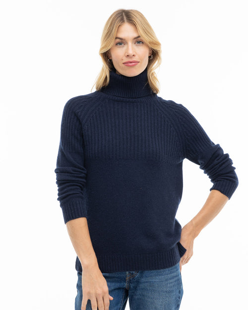 LIFESTYLE / EDITORIAL: Woman wearing navy blue ribbed turtleneck cashmere sweater and jeans against white background