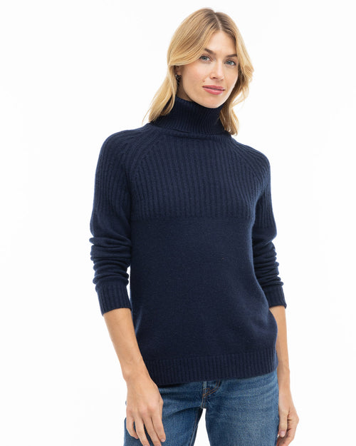 LIFESTYLE / EDITORIAL: Woman wearing navy blue turtleneck cashmere sweater and jeans against white background