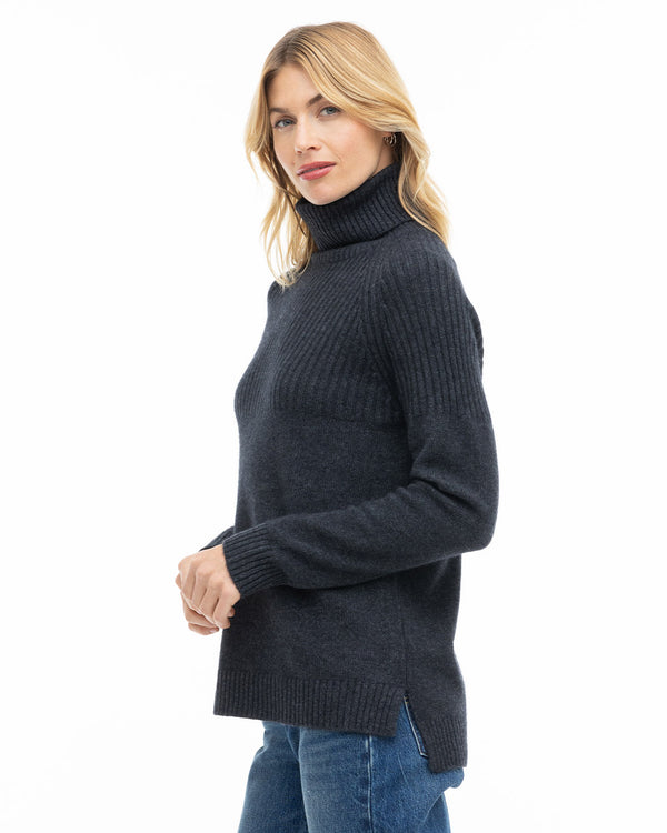 LIFESTYLE / EDITORIAL: Woman wearing charcoal turtleneck cashmere sweater and blue jeans, side view on white background