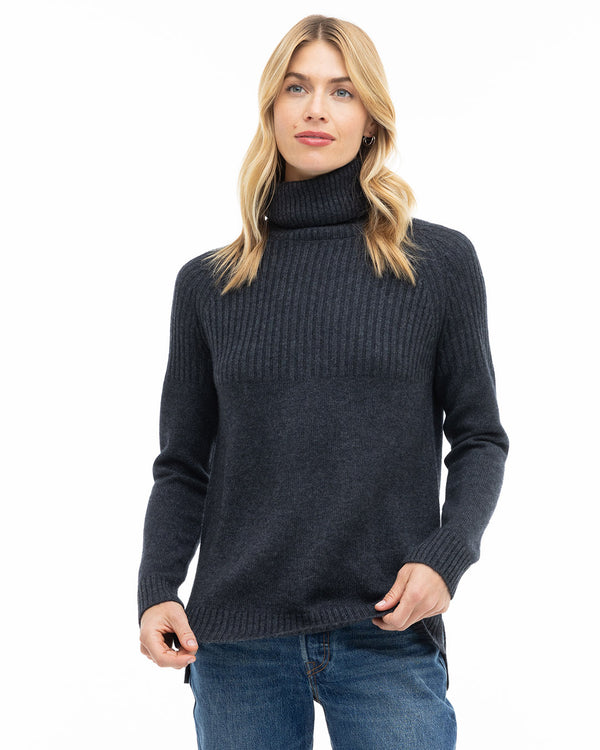 LIFESTYLE / EDITORIAL: Woman wearing charcoal ribbed turtleneck cashmere sweater with blue jeans against white background