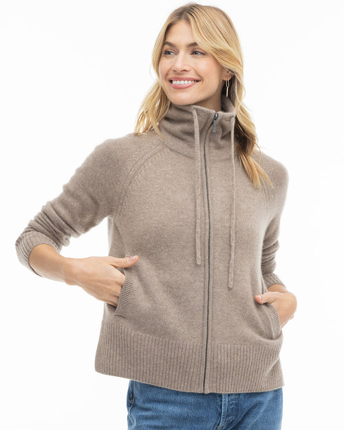 LIFESTYLE / EDITORIAL: Woman wearing a zip-up driftwood-colored cashmere sweater with hands in pockets, smiling