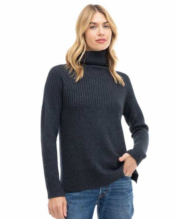 LIFESTYLE / EDITORIAL: Woman wearing charcoal ribbed turtleneck cashmere sweater with blue jeans, hand in pocket