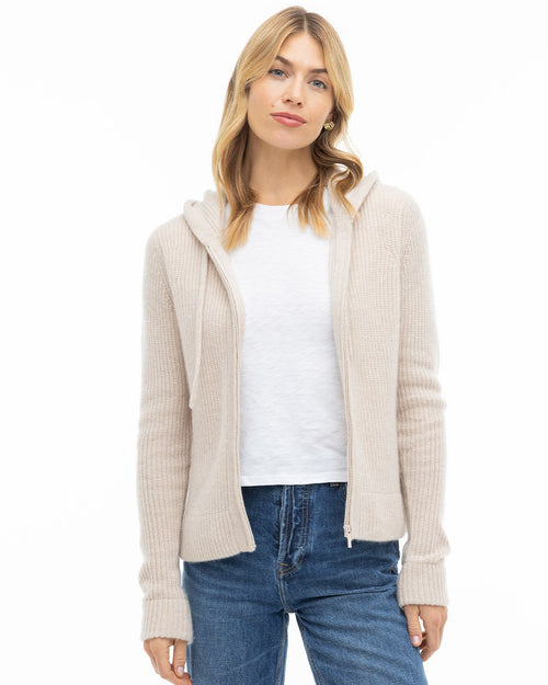 LIFESTYLE / EDITORIAL: Woman wearing oatmeal zip-up cashmere hoodie, white t-shirt, and blue jeans against white background