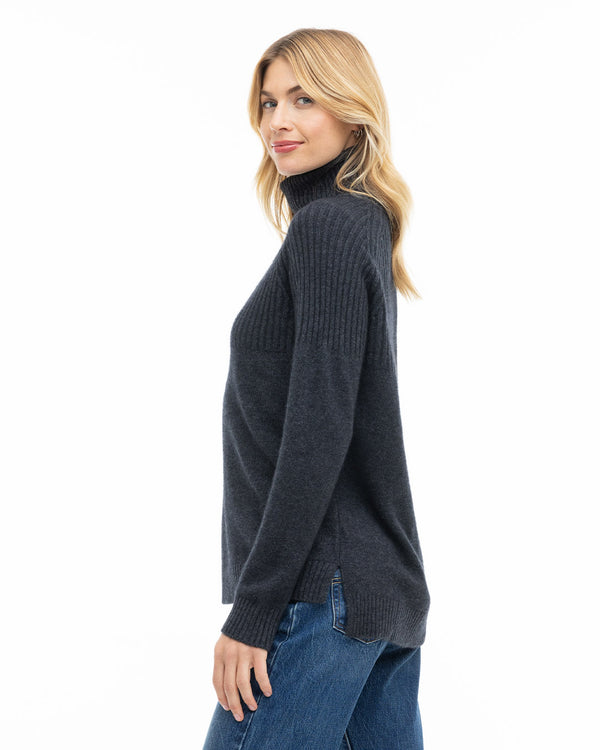 Woman in charcoal turtleneck cashmere sweater and blue jeans, side view, white background