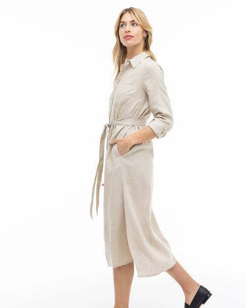Woman in beige long-sleeve belted midi dress with side slit, standing in profile against white background