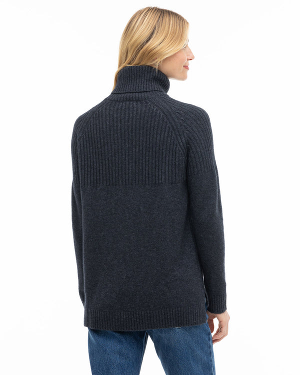 Woman wearing charcoal ribbed turtleneck cashmere sweater, back view, paired with blue jeans against white background