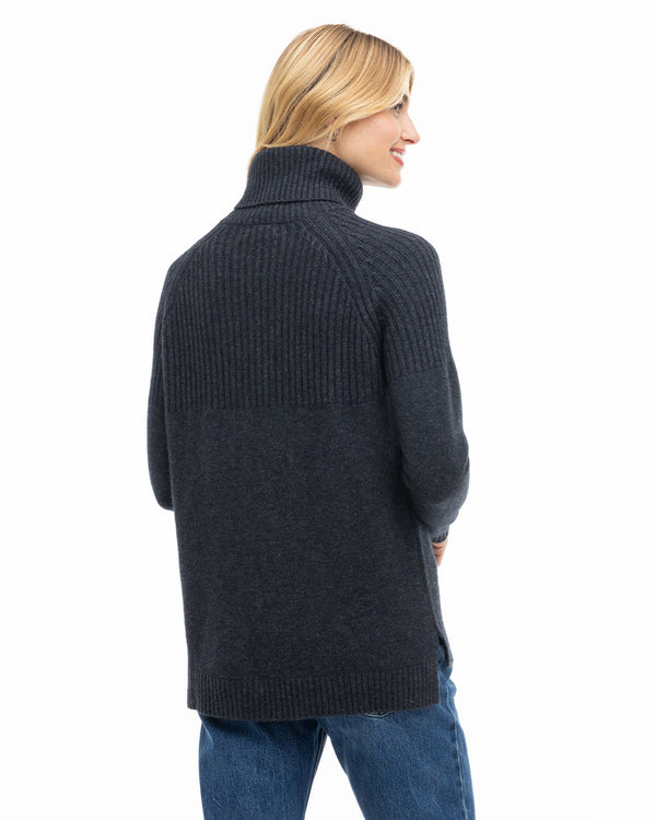 Woman wearing charcoal turtleneck cashmere sweater and blue jeans, shown from back and side profile