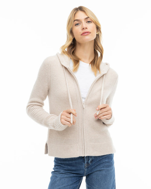 Front view image of a woman wearing an oatmeal zip-up cashmere hoodie with a white shirt and blue jeans