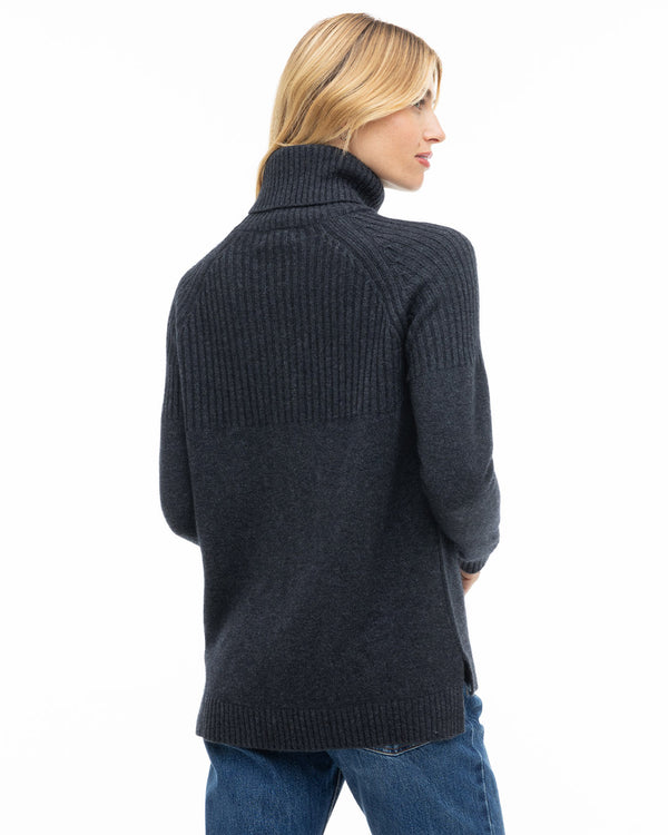 Woman wearing charcoal ribbed turtleneck cashmere sweater and blue jeans, viewed from back and side profile