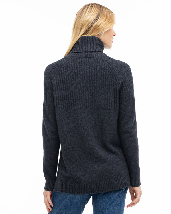 LIFESTYLE / EDITORIAL: Woman wearing charcoal ribbed turtleneck cashmere sweater, back view, paired with blue jeans