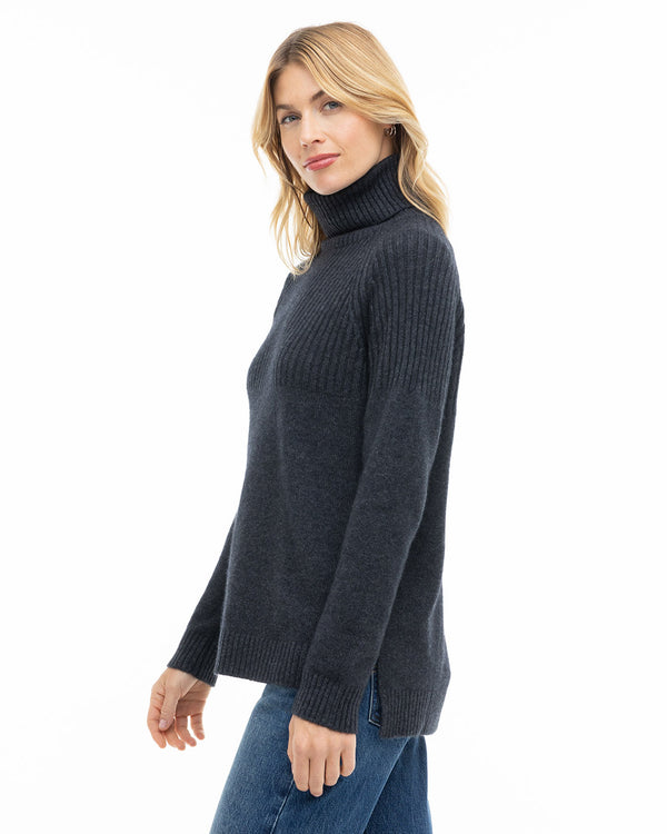 Woman wearing charcoal turtleneck cashmere sweater and blue jeans, side view, white background