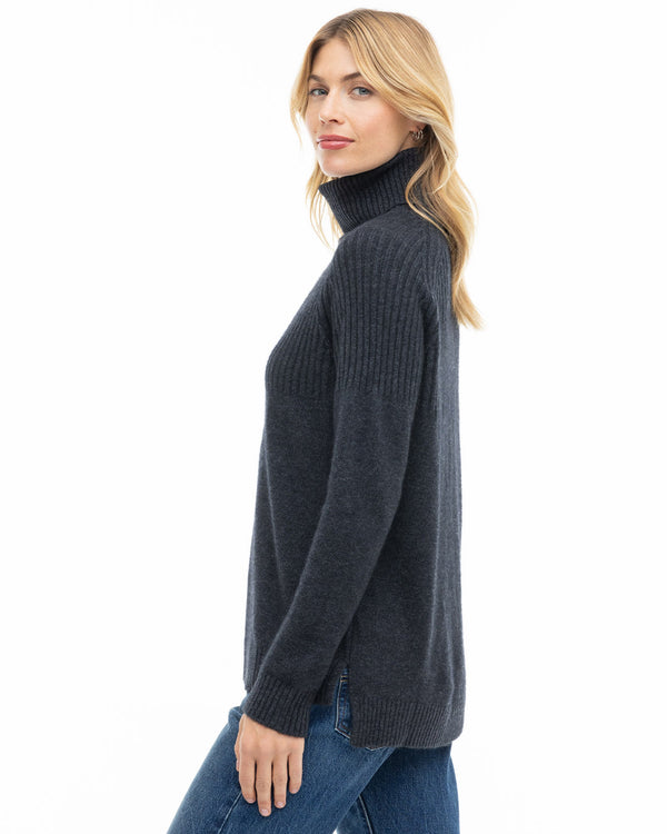 LIFESTYLE / EDITORIAL: Woman wearing charcoal turtleneck cashmere sweater and blue jeans, side view against white background