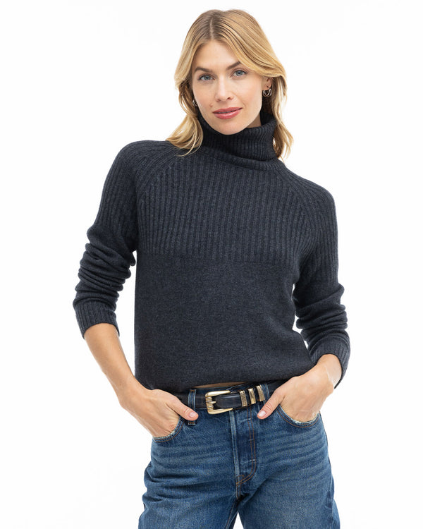 LIFESTYLE / EDITORIAL: Woman wearing charcoal ribbed turtleneck cashmere sweater and blue jeans with hands in pockets