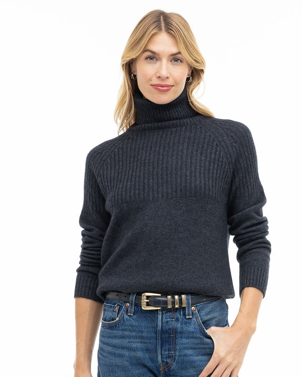 Front view image of a woman wearing a charcoal ribbed turtleneck cashmere sweater with blue jeans and black belt