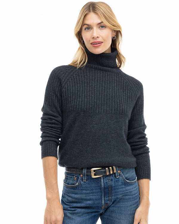 LIFESTYLE / EDITORIAL: Woman wearing charcoal ribbed turtleneck cashmere sweater and blue jeans against white background